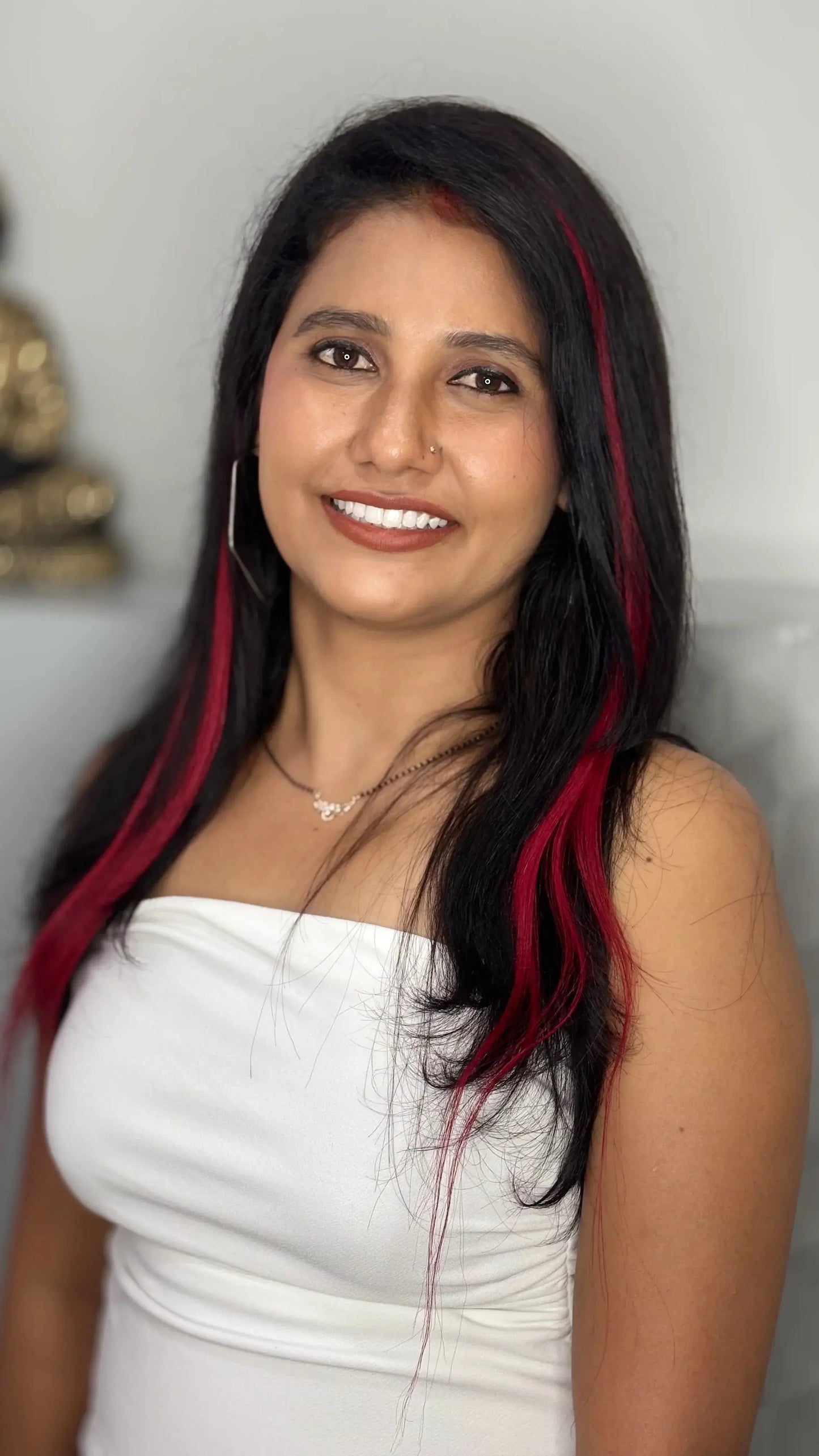 Smiling woman with long black hair and red highlights wearing a white strapless top and silver necklace