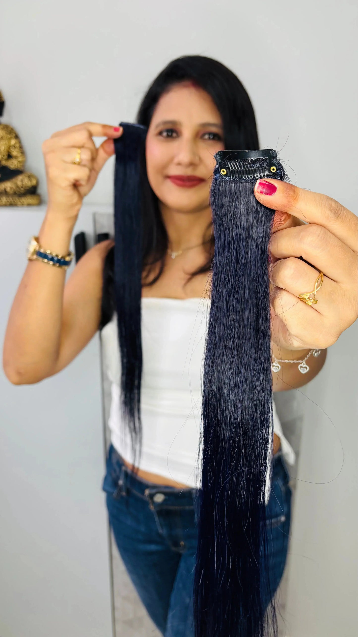Woman holding long, straight black clip-in hair extensions with shiny texture indoors