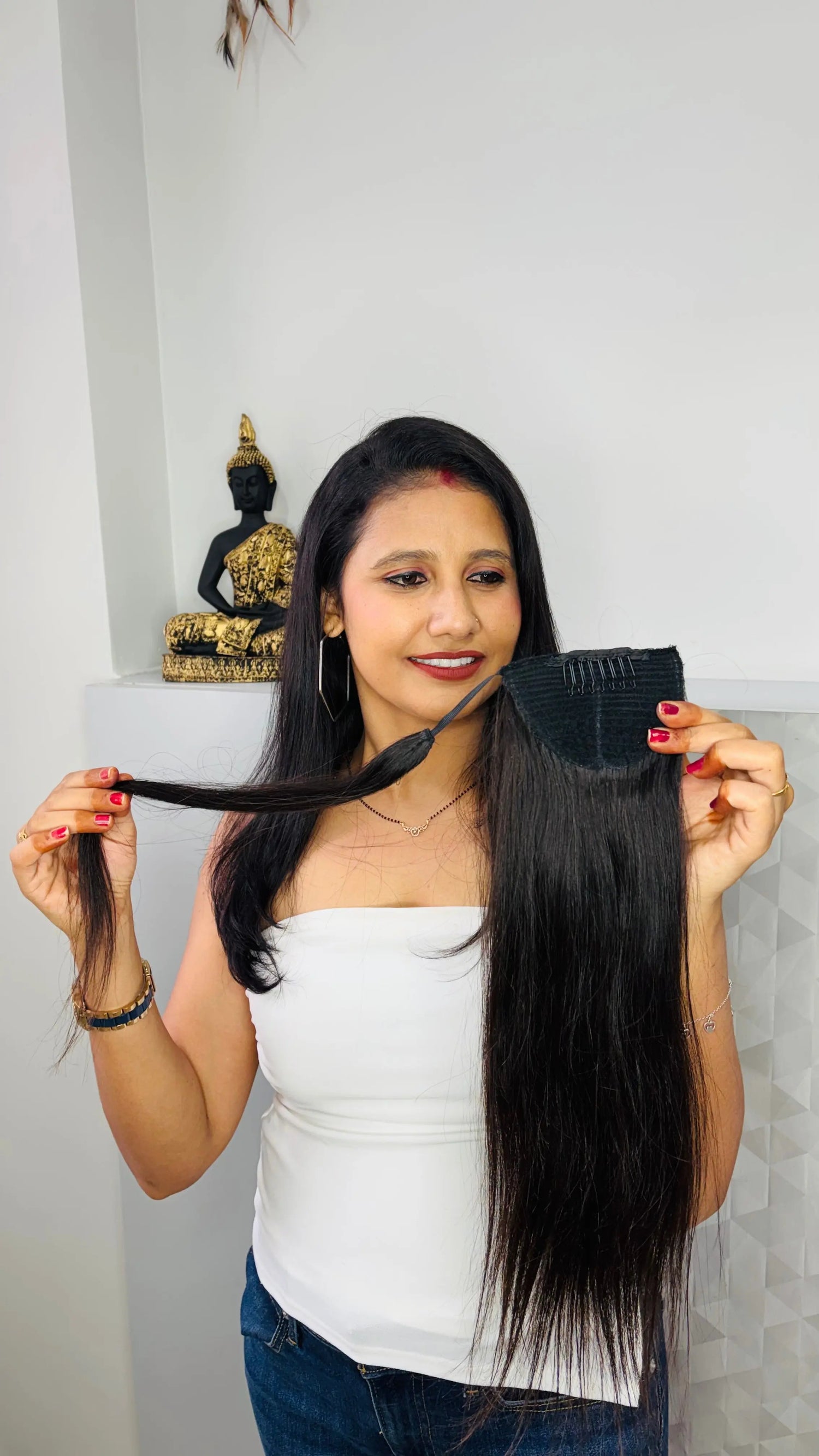Woman holding long black hair extension piece indoors with Buddha statue background