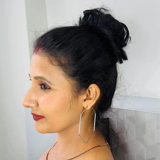 Profile of woman with black hair bun, red lipstick, nose stud, large geometric hoop earrings, and white top