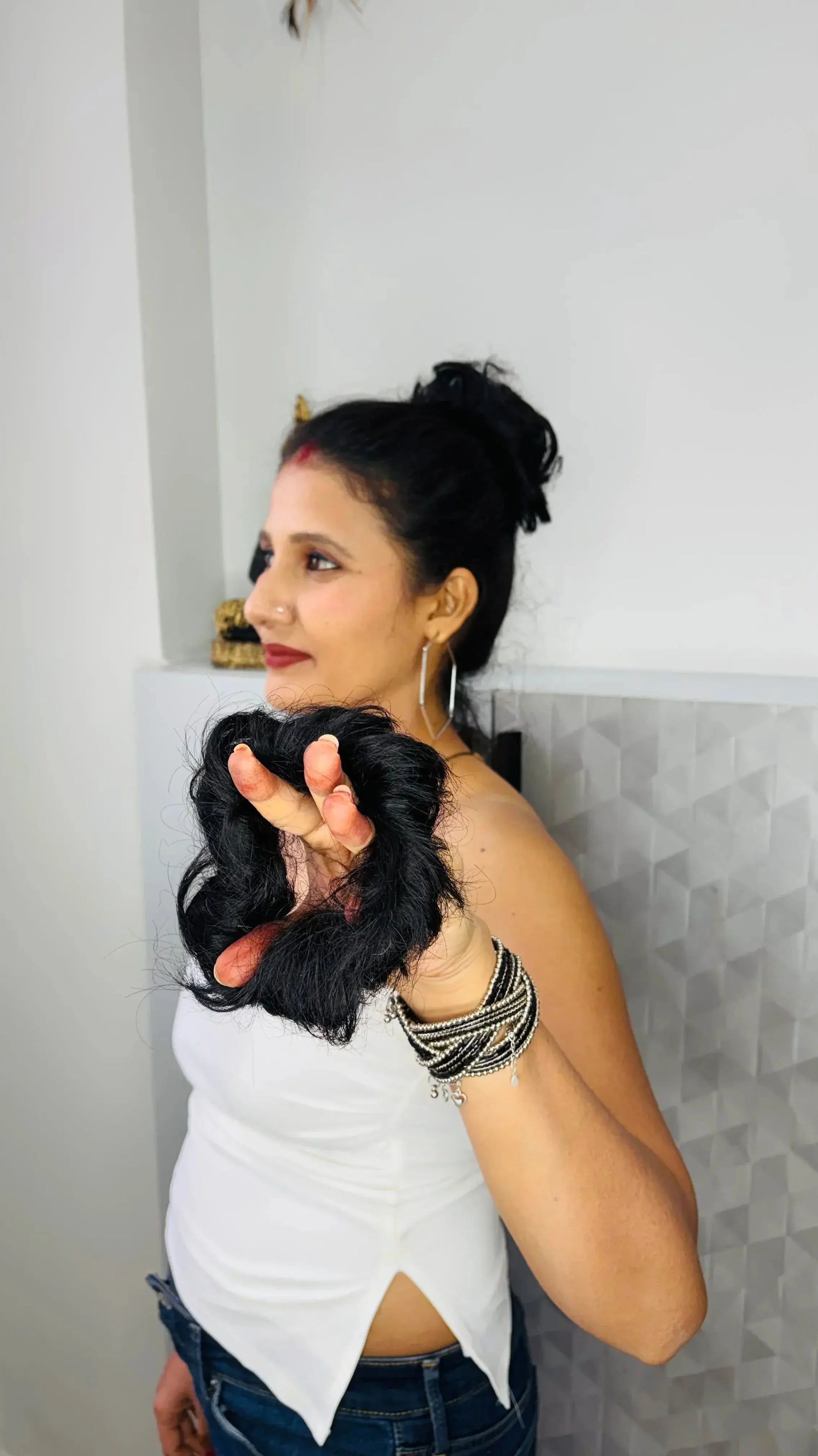 Woman holding a section of cut black hair in hand, wearing white top and bracelets indoors