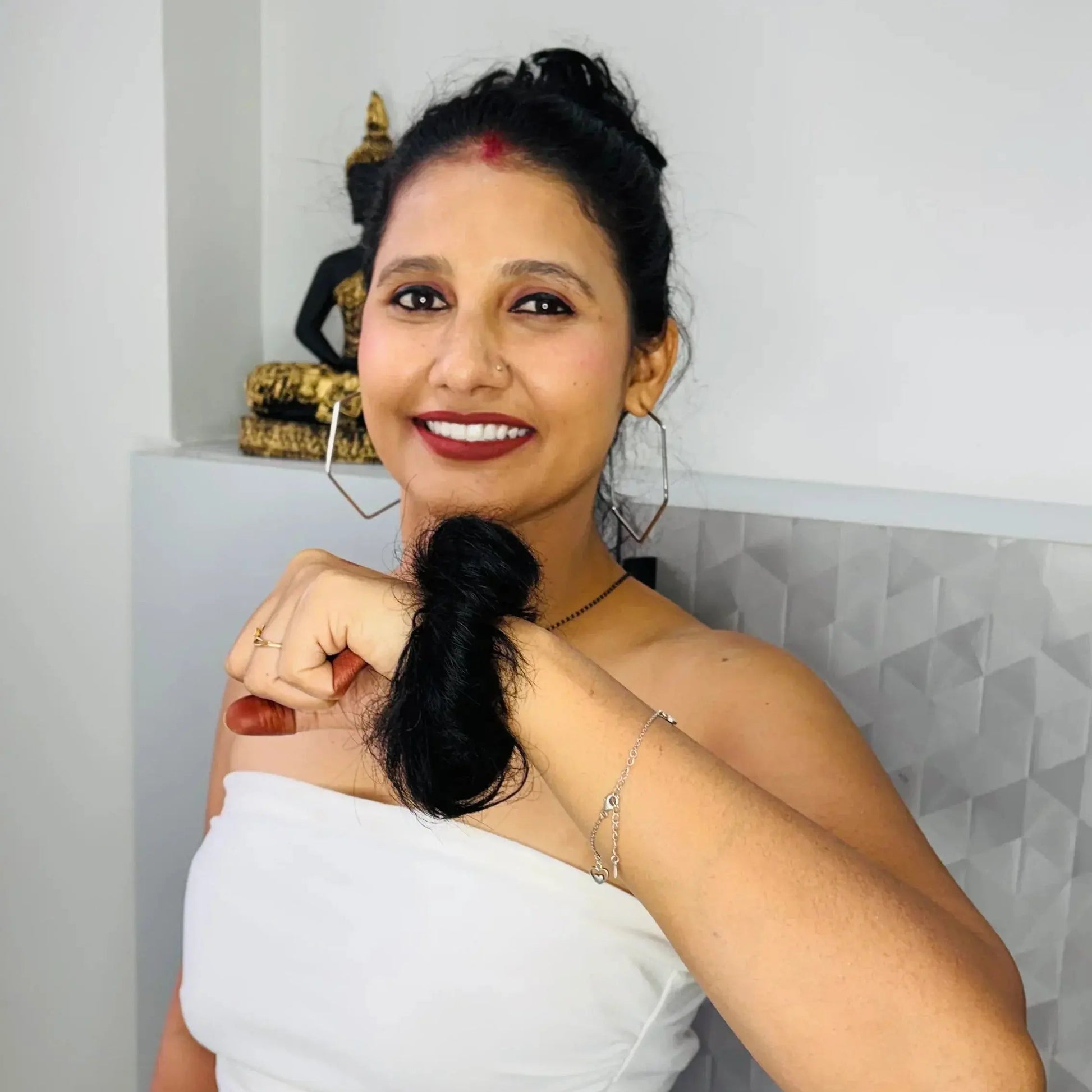 Smiling woman with dark hair in white strapless top and blue jeans, holding her ponytail indoors