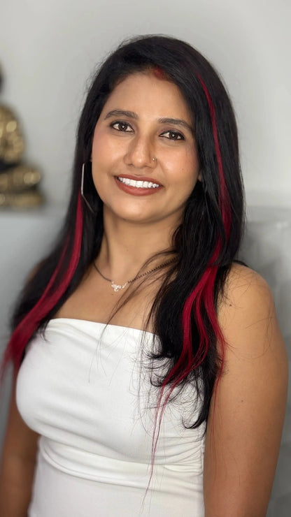 Smiling woman with long black hair and red highlights wearing a white strapless top and silver necklace