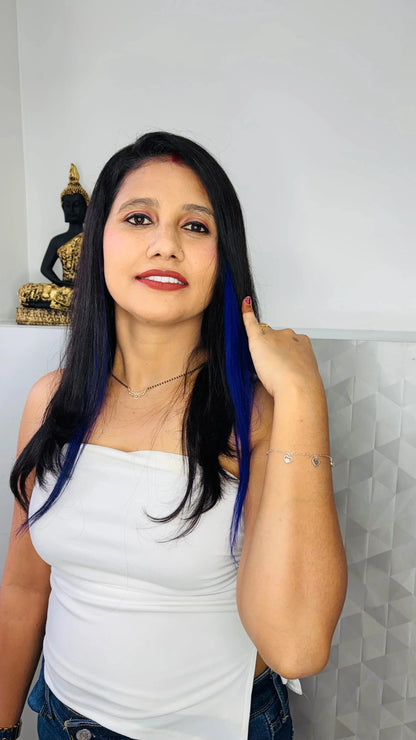 Woman with long black hair with blue streaks wearing white top and silver heart bracelet, Buddha statue background