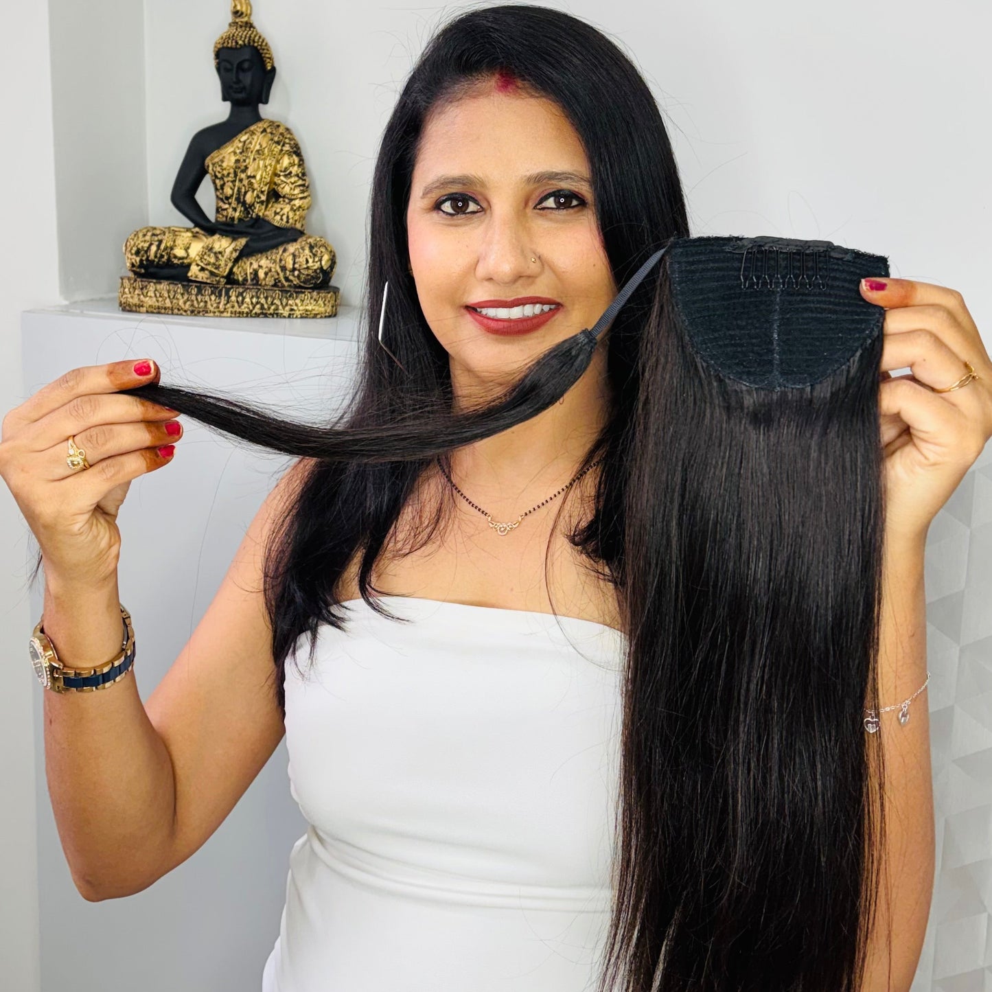 Woman holding a hair extension with a white wall and Buddha statue in the background